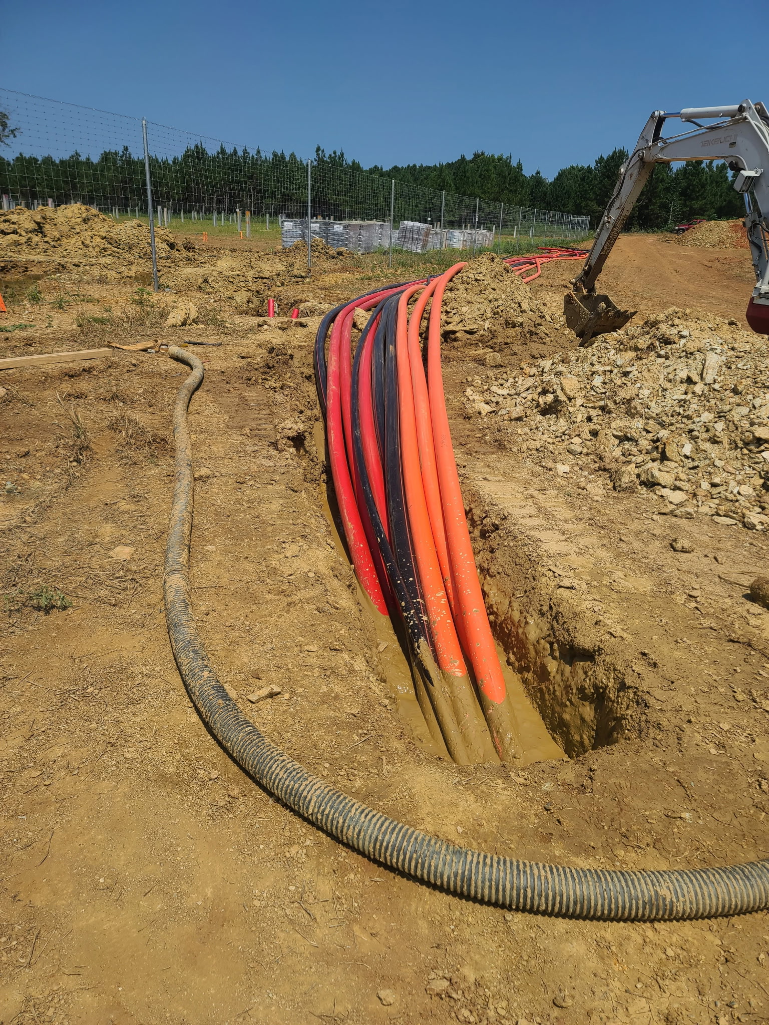 Bundle of orange and black electrical and communication conduit laid into an open trench on a Triple J Specialist job site