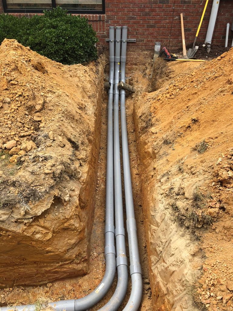 Excavated trench with utility conduit laid in along a building foundation on a Triple J Specialist job site