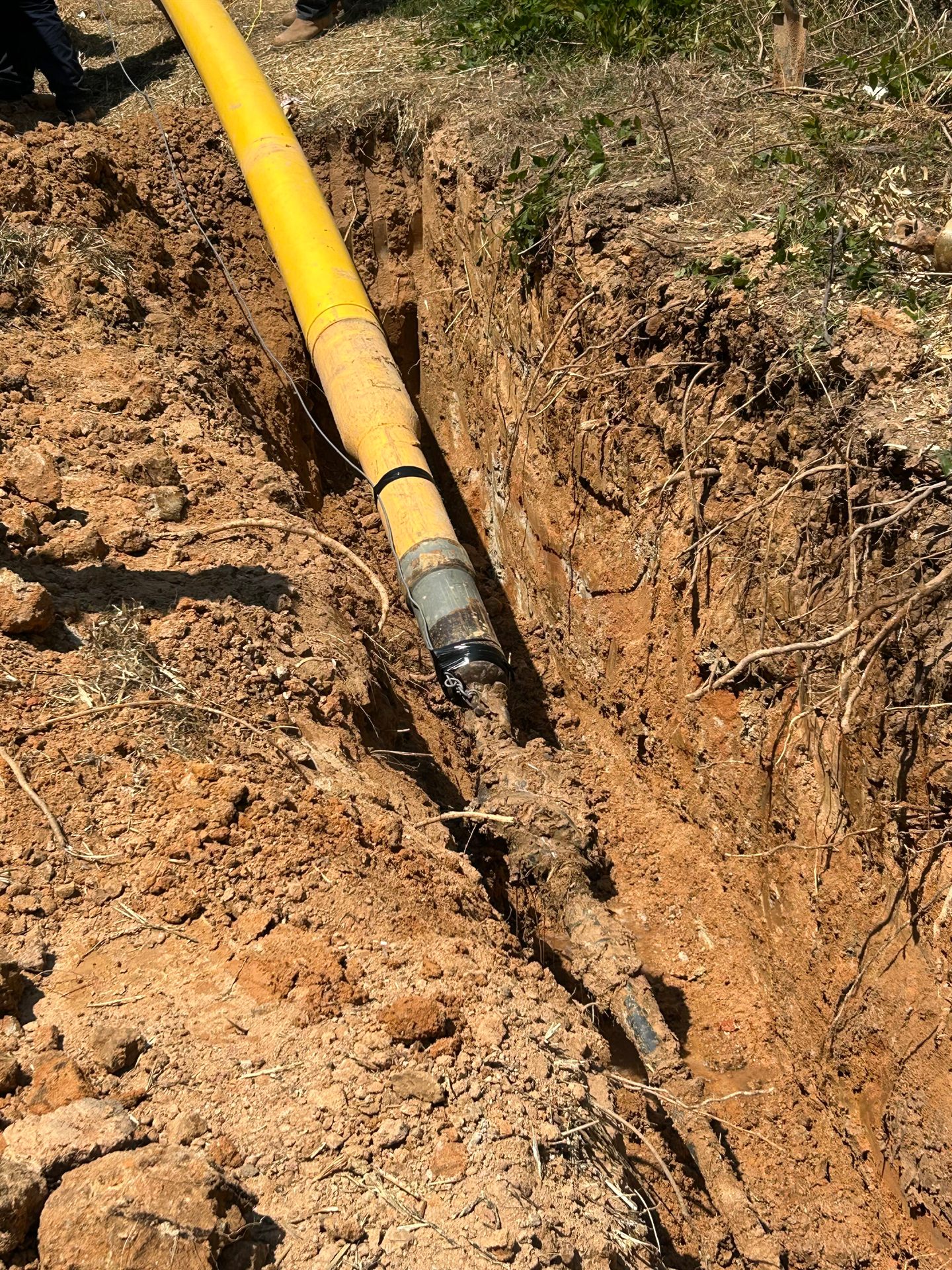Yellow polyethylene gas line connected to the drill head during pullback through an excavated bore pit
