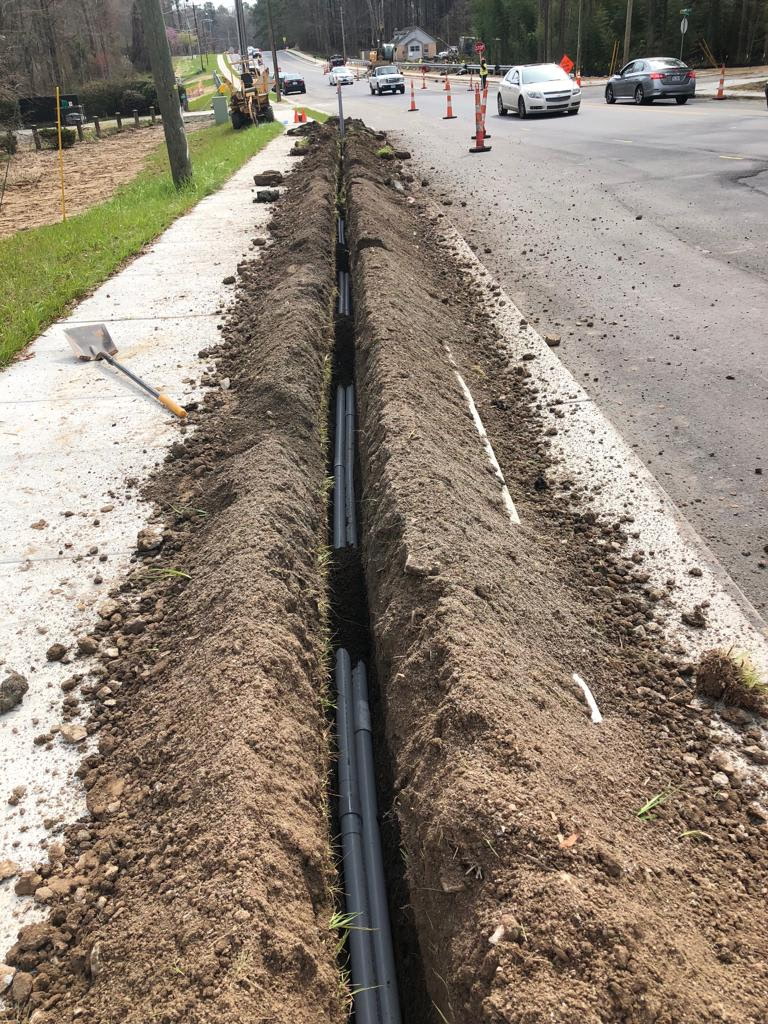 Utility line being laid into a roadside trench along a residential street